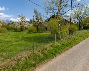 Grünes Grundstück mit blühenden Bäumen und Blick auf die umliegende Landschaft und Berge unter blauem Himmel.