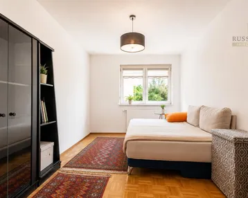 Helles Schlafzimmer mit Einzelbett, Parkettboden und Blick ins Grüne.