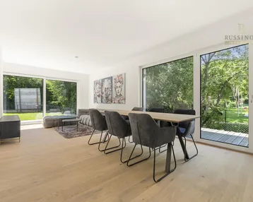 Heller, offener Wohn- und Essbereich mit Holzboden und großen Fenstern zum Garten.