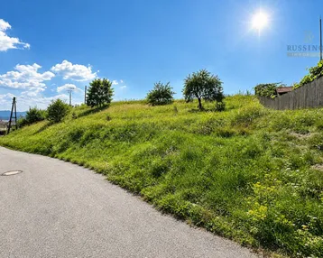 Grünes Grundstück am Hang mit asphaltierter Straße und sonnigem Himmel.