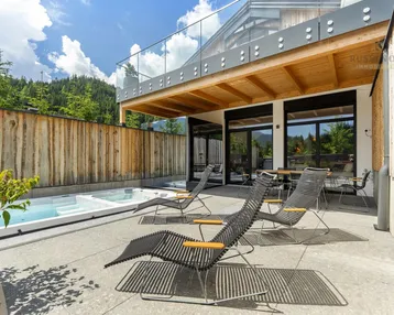 Geräumige Terrasse mit Whirlpool, Liegestühlen und Essbereich, umgeben von einer Holzwand und Bergblick.