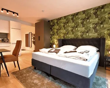 Modernes Schlafzimmer mit Doppelbett, auffälliger Tapete und integrierter Küchenzeile.