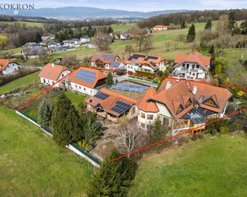 Luftaufnahme eines weitläufigen Anwesens mit mehreren Gebäuden, umgeben von grünen Hügeln und mit Solaranlagen auf den Dächern.