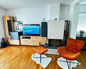 Helles Wohnzimmer mit Holzboden, Kamin und modernen Möbeln in warmen Farben.