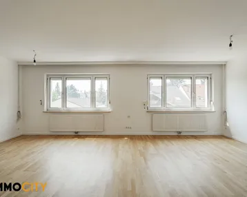 Helles, leeres Zimmer mit Parkettboden und zwei Fenstern, bereit zur individuellen Gestaltung.