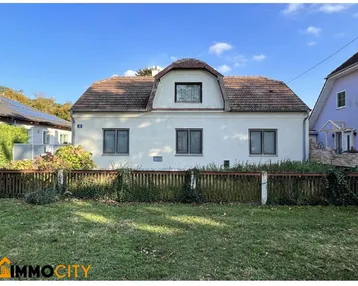 Vorderansicht eines Einfamilienhauses mit Gartenbereich und traditionellem Ziegeldach unter blauem Himmel.