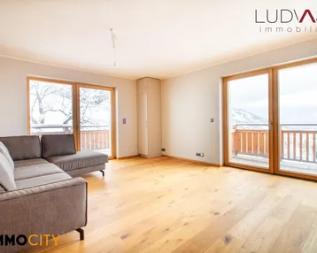 Helles Wohnzimmer mit modernem Sofa, Holzboden und Zugang zu einem Balkon mit Bergblick.