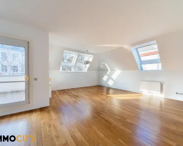 Helles Dachgeschosszimmer mit Holzboden, Dachfenstern und Zugang zu einem kleinen Balkon.