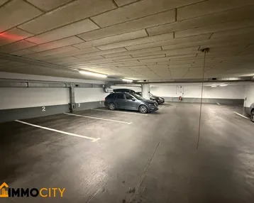 Tiefgarage mit mehreren markierten Stellplätzen und geparkten Fahrzeugen, gut beleuchtet.