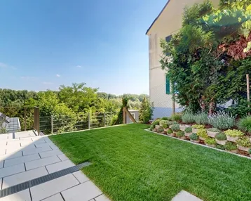 Gepflegter Gartenbereich mit Rasenfläche, gepflasterter Terrasse und Blick ins Grüne.
