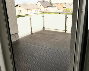 Geräumiger Balkon mit Holzdielenboden und Glasgeländer, bietet einen Blick auf die Umgebung.
