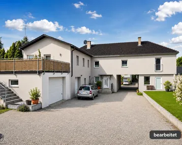 Großes Wohnhaus mit Garage, Balkon und gepflegter Kiesauffahrt unter blauem Himmel.