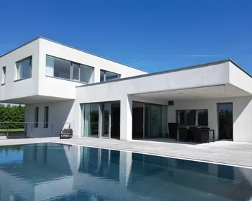 Moderne weiße Villa mit Flachdach, großem Swimmingpool und überdachter Terrasse unter blauem Himmel.