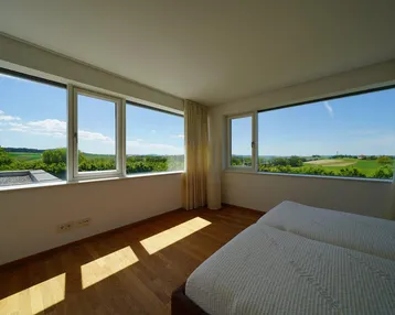 Helles Schlafzimmer mit Holzboden und Panoramafenstern, die einen weiten Blick über die Landschaft bieten.