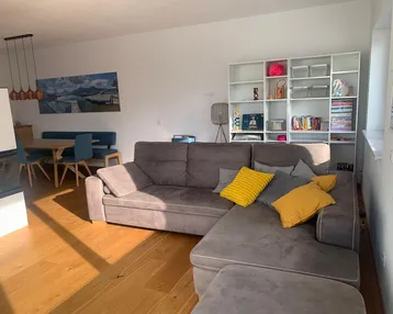 Heller offener Wohn- und Essbereich mit gemütlichem Sofa, Kamin und Holzboden.