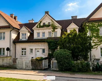 Historische Fassade eines charmanten Hauses mit üppigem Grün und traditionellem Zaun.