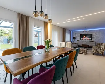 Moderner offener Wohn- und Essbereich mit großem Holztisch und Zugang zum Garten.