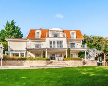 Großzügige Villa mit weitläufigem Garten, Pool und mehreren Balkonen unter blauem Himmel.