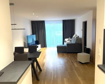 Helles, offenes Wohnzimmer mit Holzboden, Sofa und Zugang zu einem Balkon.