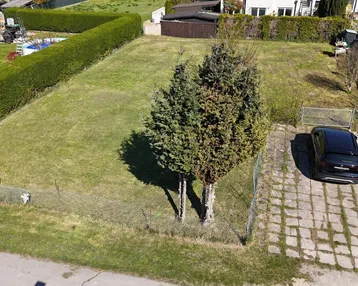 Luftaufnahme eines unbebauten Grundstücks mit Zufahrt, Rasenfläche und umgebenden Gärten.