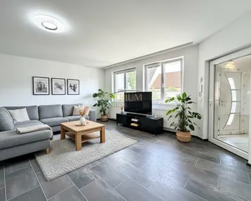 Helles Wohnzimmer mit modernem Sofa, Holztisch und dunklen Fliesen, durch große Fenster gut belichtet.