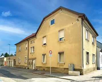 Gebäudeansicht eines älteren Mehrfamilienhauses mit gelber Fassade und Fenstern zur Straße hin.