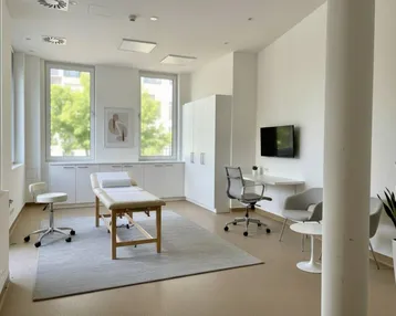 Heller Behandlungsraum mit großen Fenstern, moderner Einrichtung und viel Tageslicht, ideal für Therapien oder Bürozwecke.