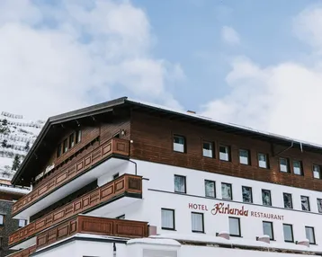 Ansicht des Hotels Kirlana mit traditioneller Holzfassade und schneebedeckten Bergen im Hintergrund.