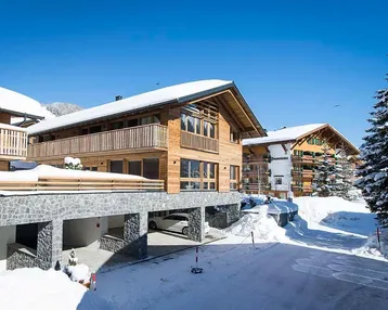 Modernes Holzchalet mit Steinsockel und Balkonen, umgeben von Schnee und Bergen.