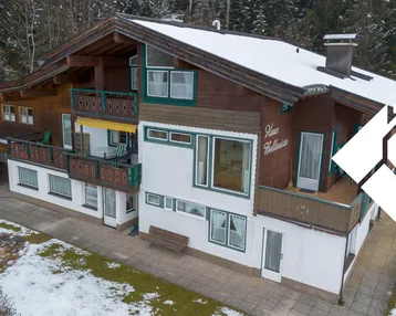 Traditionelles Alpenhaus mit mehreren Holzbalconen, schneebedecktem Dach und umgeben von Wald.