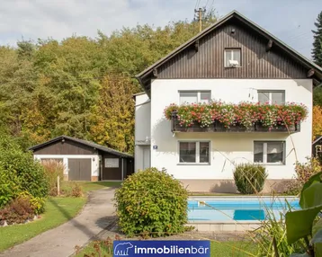 Charmantes Einfamilienhaus mit Balkon, Garten, Pool und separater Garage, umgeben von viel Grün.
