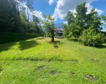 Weitläufiger Garten mit Rasenfläche, alten Bäumen und malerischem Bergblick im Hintergrund.