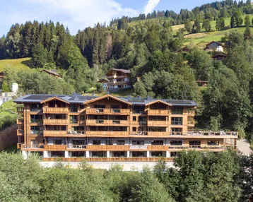 Modernes Apartmentgebäude in den Bergen mit Holzfassade und vielen Balkonen.