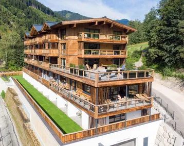 Modernes Holzgebäude mit mehreren Balkonen und Terrassen in alpiner Berglandschaft.