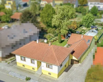 Luftaufnahme eines Einfamilienhauses mit gelb-weißer Fassade, rotem Ziegeldach, Garten und Pool.
