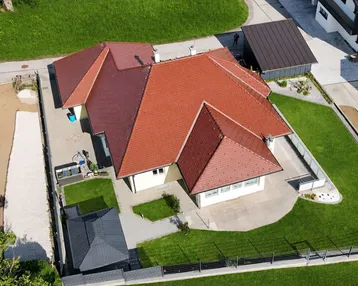 Luftaufnahme eines Hauses mit rotem Ziegeldach, gelber Fassade und gepflegtem Garten.
