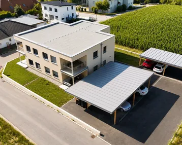 Luftaufnahme eines modernen Wohngebäudes mit Flachdach und Carports neben einem grünen Feld.