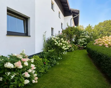 Gepflegter Gartenbereich mit blühenden Hortensien und Rasenfläche entlang der Hausfassade.