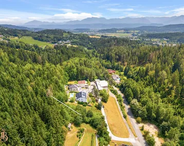 Panoramablick auf das Grundstück, eingebettet in eine grüne Landschaft mit Bergen am Horizont.