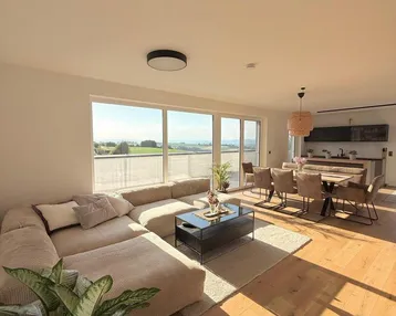Helles, offenes Wohn-Esszimmer mit großem Sofa, Holzboden und weitem Blick ins Grüne.