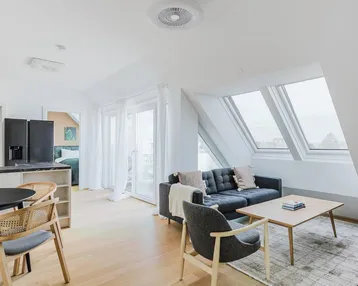 Helles Wohn- und Esszimmer mit Dachschrägen, modernen Möbeln und Zugang zu weiteren Räumen.