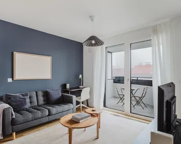 Modernes Wohnzimmer mit dunkelblauer Akzentwand, Sofa, Schreibtisch und Zugang zum Balkon.