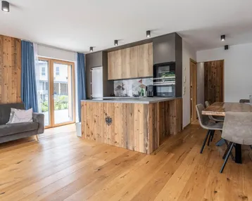 Offener Wohn-Essbereich mit integrierter Holzküche, Holzboden und Zugang zu einer Terrasse.