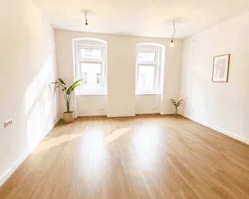 Heller, leerer Raum mit Laminatboden und zwei Fenstern, ideal als Wohnzimmer.