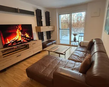 Gemütliches Wohnzimmer mit bequemer Ledercouch, Holzboden und Zugang zur Terrasse.