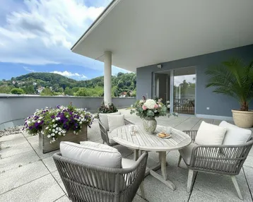 Geräumige Terrasse mit Sitzgelegenheiten, Blumenkästen und weitem Blick auf die grüne Umgebung.