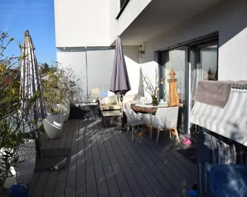 Geräumiger Balkon mit Holzboden, Sitzgelegenheiten und Pflanzen, ideal zum Entspannen im Freien.
