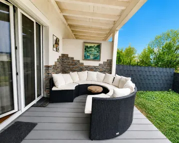 Überdachte Terrasse mit bequemen Outdoor-Möbeln, Holzboden und direktem Zugang zum Garten.