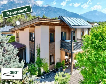 Modernes Haus mit Holzfassade, Balkon, großer Holzterrasse und beeindruckendem Bergblick.