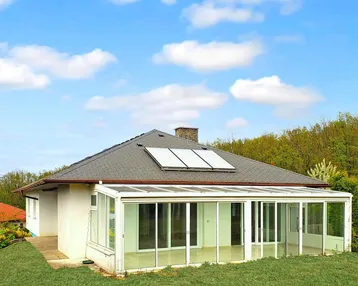 Rückseite des Hauses mit großem Wintergarten, Solaranlage auf dem Dach und Garten.